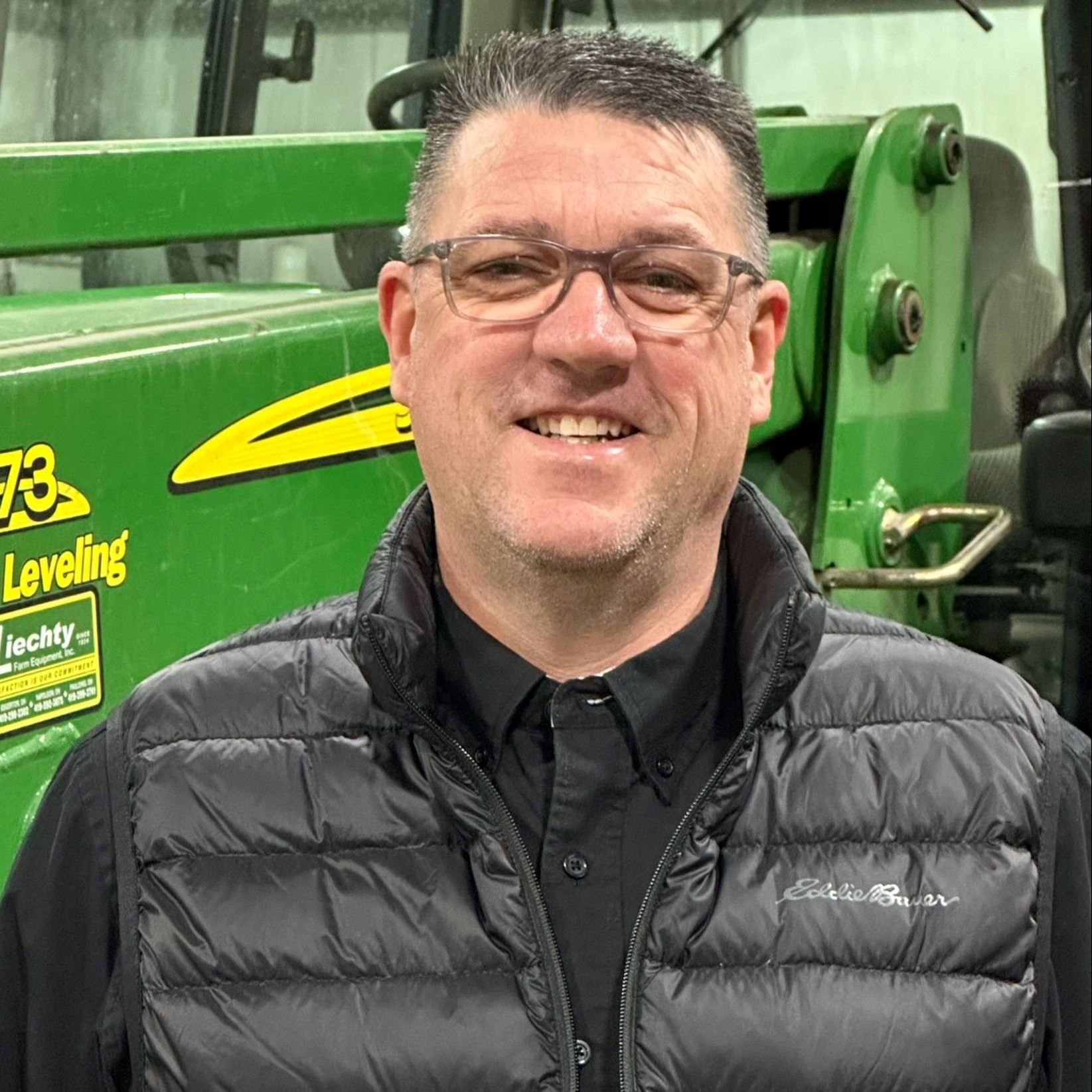 man in vest standing in front of tractor